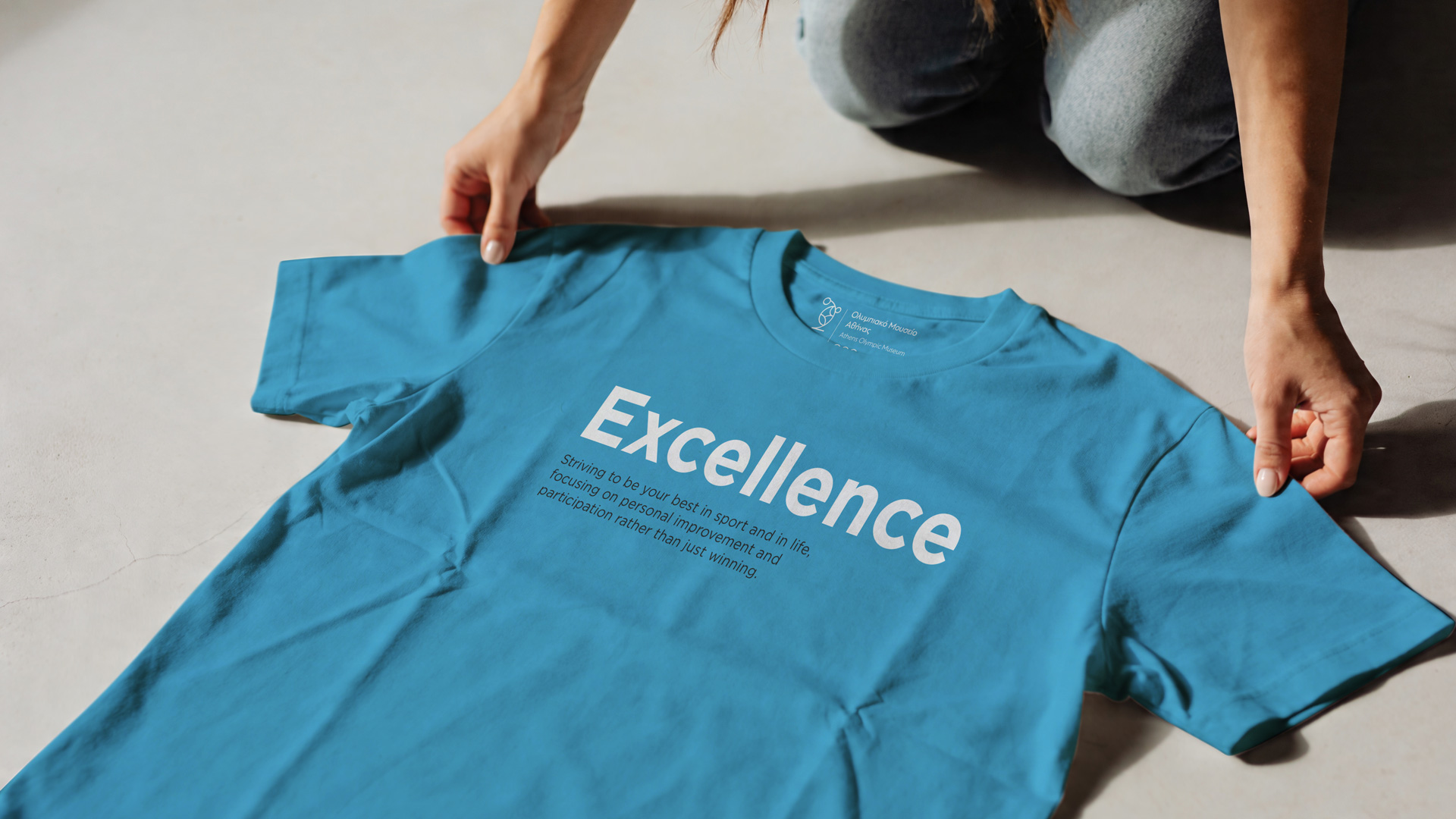 olympic-museum-1.jpg: Hands unfolding a light blue t-shirt printed with the word 