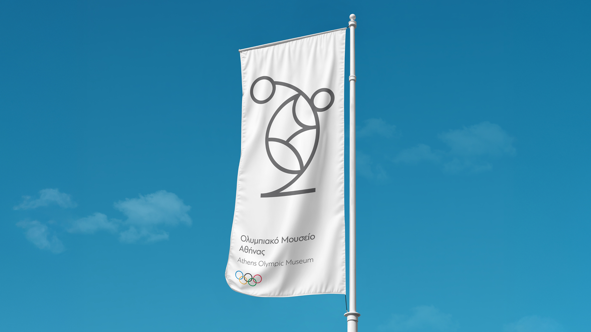 A white vertical flag waving against a blue sky, displaying the grey abstract discus thrower logo and Athens Olympic Museum text.