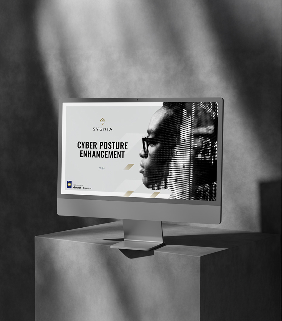 A sleek desktop monitor displaying the title slide of a Sygnia presentation titled 'Cyber Posture Enhancement', featuring double exposure portrait imagery.